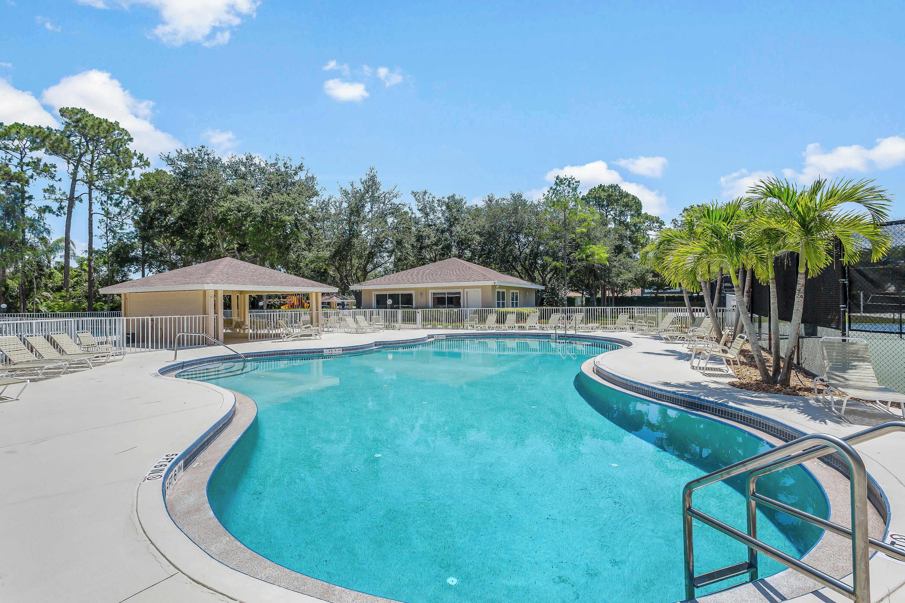 A swimming pool with a curved edge, surrounded by lounge chairs and a covered area.