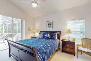 Ein Schlafzimmer mit einem Bett, einem Nachttisch, einem Sessel, einem Deckenventilator und einem Fenster.