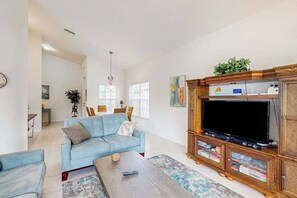 A living room with a sofa, coffee table, TV stand, and a dining area in the background. - Waterfront Home with Private Pool & Great Views - Close to Golf & Naples Beach (Naples)