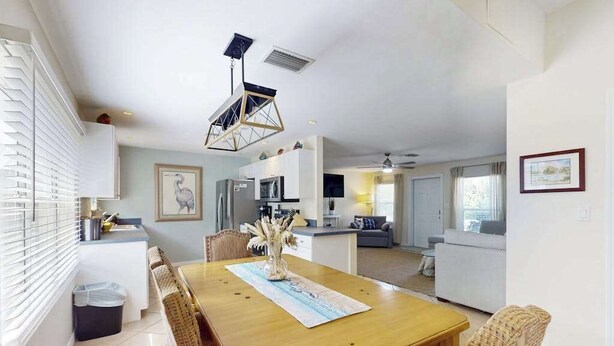A modern kitchen with white cabinets, a dining area with a wooden table and wicker chairs, and a living area with a sofa and a TV. - Charming home w/ guest house- near the beach - spacious yard with patio (Bonita Springs)