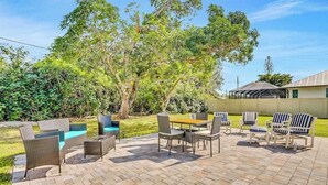 An outdoor patio with wicker furniture, a wooden table, and a pool. - Charming home w/ guest house- near the beach - spacious yard with patio (Bonita Springs)