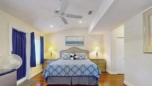A bedroom with a bed, a ceiling fan, two bedside lamps, a nightstand, and a window with curtains. - Charming home w/ guest house- near the beach - spacious yard with patio (Bonita Springs)