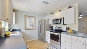 A modern kitchen with white cabinets, a stainless steel refrigerator, a microwave, an oven, and a sink. - Charming home w/ guest house- near the beach - spacious yard with patio (Bonita Springs)
