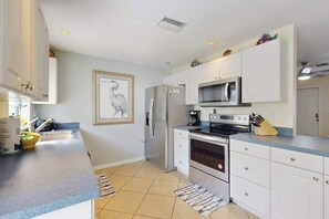 A modern kitchen with white cabinets, a stainless steel refrigerator, a microwave, an oven, and a sink. - Charming home w/ guest house- near the beach - spacious yard with patio (Bonita Springs)