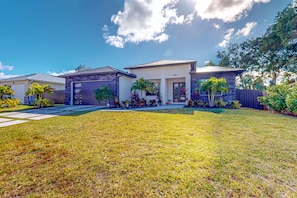A modern two-story house with a well-maintained lawn, a garage, and a front porch with potted plants.
