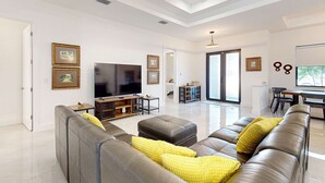 Ein modernes Wohnzimmer mit einem großen Flachbildfernseher, Ledersofas und einem Essbereich mit Tisch und Stühlen.