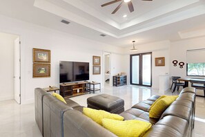 A modern living room with a large flat-screen TV, leather sofas, and a dining area with a table and chairs.