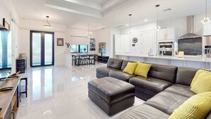 Ein modernes Wohnzimmer mit Ecksofa, Essbereich und Küche mit weißen Schränken und integriertem Backofen.