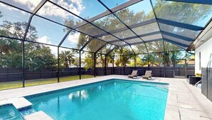 Ein Schwimmbecken mit überdachtem Bereich, umgeben von einem Zaun, und ein Haus im Hintergrund.