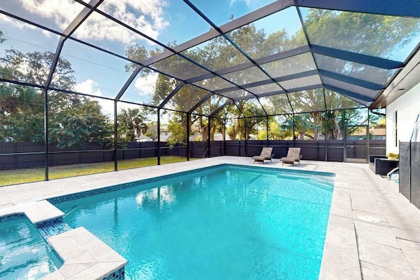 A swimming pool with a covered area, surrounded by a fence, and a house in the background.