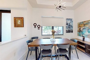 A dining area with a wooden table, six chairs, a modern chandelier, and artwork on the walls.