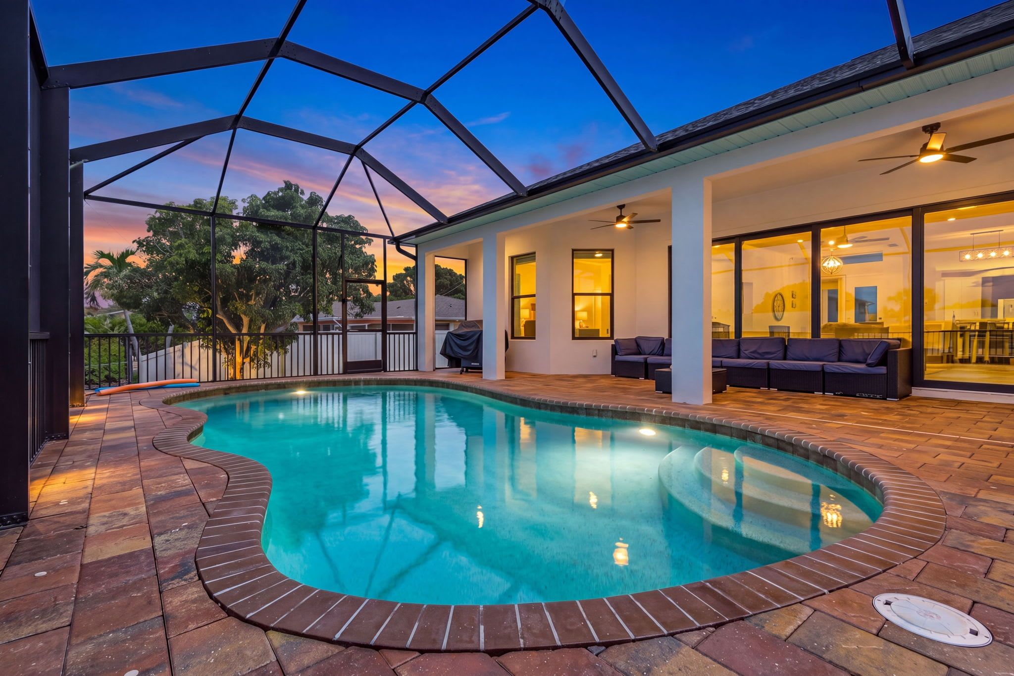 Una piscina de borde curvo, rodeada por un patio con mobiliario exterior y una zona de barbacoa techada.