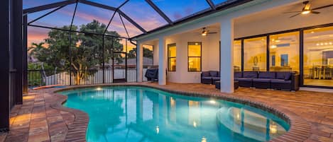 A swimming pool with a curved edge, surrounded by a patio area with outdoor seating and a covered barbecue area.