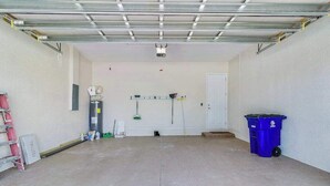 Eine Garage mit Betonboden, einer weißen Tür, einem blauen Mülleimer und einer Leiter.