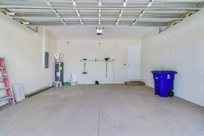 Eine Garage mit Betonboden, einer weißen Tür, einem blauen Mülleimer und einer Leiter.