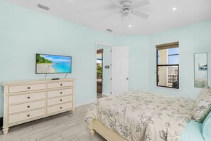 Ein Schlafzimmer mit Bett, Kommode, Fernseher und Deckenventilator.