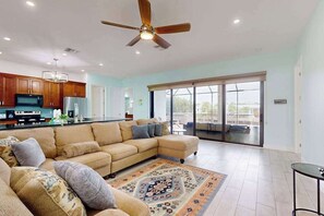 A spacious living area with a large sectional sofa, a ceiling fan, and a view through a sliding glass door to an outdoor patio. - Spacious, dog friendly home with pool, on waterway within minutes to the Gulf (Bokeelia)
