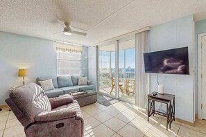 A living room with a sofa, a recliner, a TV, and a balcony with a view. - Gulf view studio with shared pool, steps to the beach, and internet (Bonita Springs)