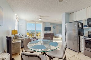 A modern kitchen with a refrigerator, microwave, and oven. There is a dining area with a glass table and chairs. The room has a large window with a view. - Gulf view studio with shared pool, steps to the beach, and internet (Bonita Springs)