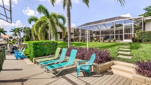 A deck with lounge chairs, a covered patio, and a building with large windows. - Canal-front home w/ private pool, hot tub, dock & kayaks/paddleboards -1 dog OK (Cape Coral)