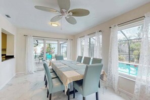 Ein Essbereich mit einem Tisch für sechs Personen, einem Deckenventilator und großen Fenstern mit Vorhängen.
