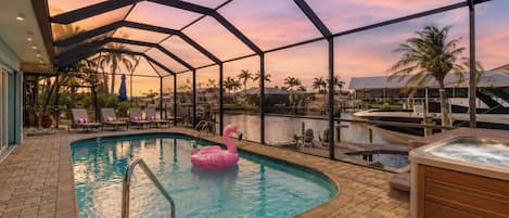 En pool med en rosa uppblåsbar flamingofigur, ett bubbelbad och utsikt över en småbåtshamn med båtar och palmer.