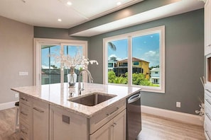 A kitchen with a large island, double sink, and a view of neighboring buildings. - Immaculate home w/ in ground outdoor pool, breezy private balcony, & pool table (Bonita Springs)