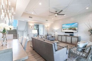 A modern living room with a sofa, coffee table, and TV. There is a staircase leading to another level. - Immaculate home w/ in ground outdoor pool, breezy private balcony, & pool table (Bonita Springs)