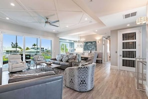 A spacious living room with a large window, a ceiling fan, and a dining area with a chandelier. - Immaculate home w/ in ground outdoor pool, breezy private balcony, & pool table (Bonita Springs)