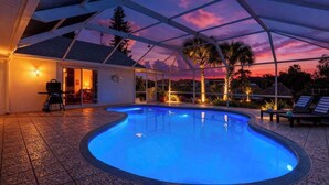 Uma piscina com área coberta, churrasqueira e espreguiçadeiras.