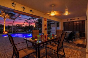 An indoor dining area with a pool view, wooden chairs, a ceiling fan, and a sunset view through a glass wall. - Canal-side gem with screened pool, boat dock & Gulf access - near dining (Cape Coral)