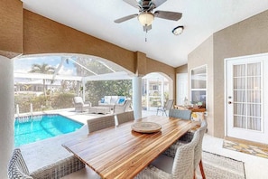 A covered patio with a pool, wicker furniture, and a ceiling fan. - Canal-front home with private heated pool, pool spa, dock, kayaks, grill, 1 bike (Cape Coral)