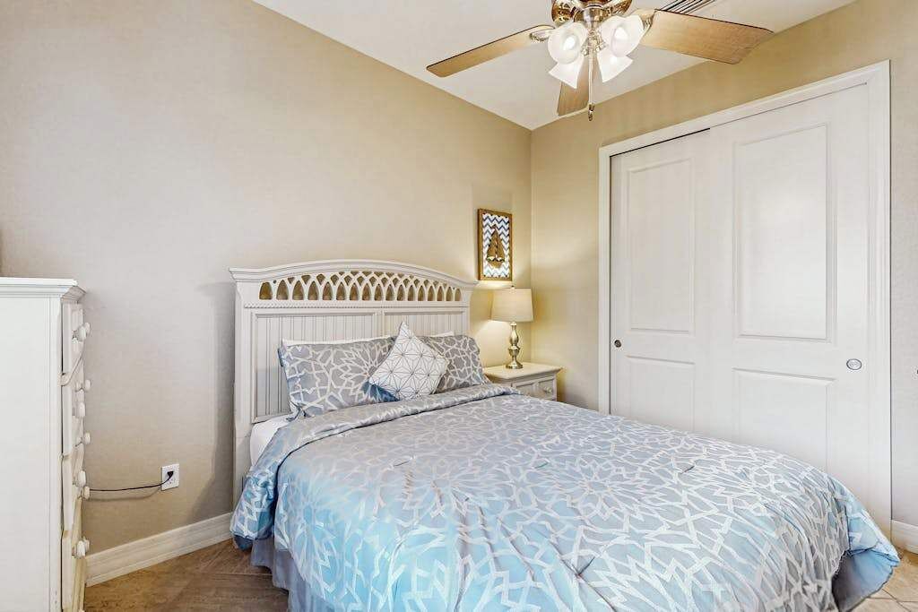 Ein Schlafzimmer mit Bett, Deckenventilator, Nachttisch mit Lampe und Tür.