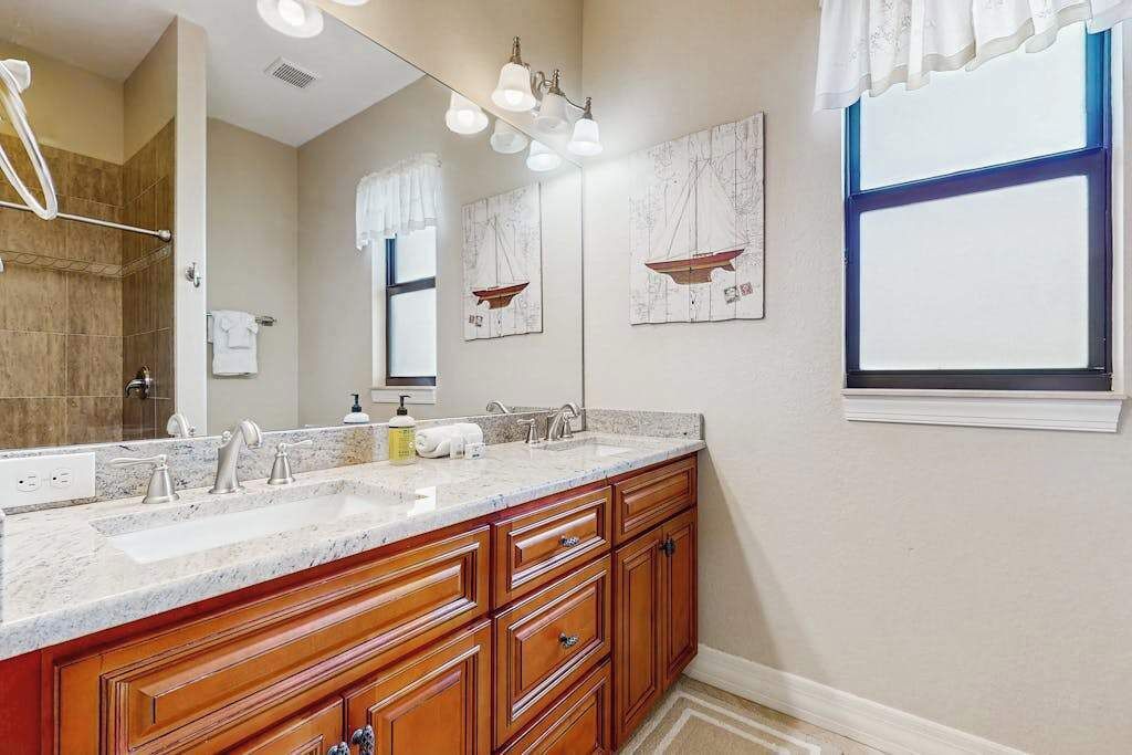 A bathroom with a double sink vanity, wooden cabinets, a large mirror, and nautical-themed wall art.