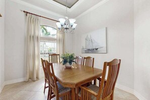 Ein Esszimmer mit Holztisch, Stühlen, einer Chandelierleuchtre, einem Topfpflanzen und einem Gemälde mit einem Segelboot.