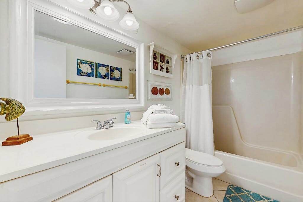 A bathroom with a white sink, a toilet, a shower with a curtain, and wall-mounted shelves with decorative items.