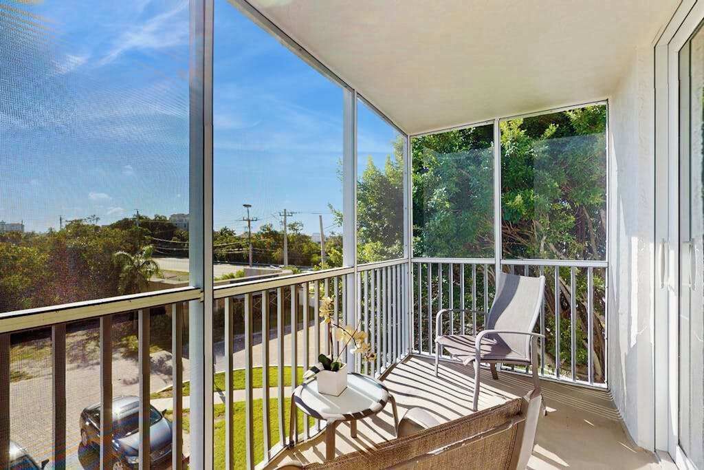 Un balcone con vista su un parcheggio e aree verdi, una sedia bianca e un tavolino con una pianta.