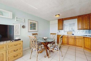 Una cocina con armarios de madera, una mesa de comedor con sillas, un televisor y cuadros en la pared.