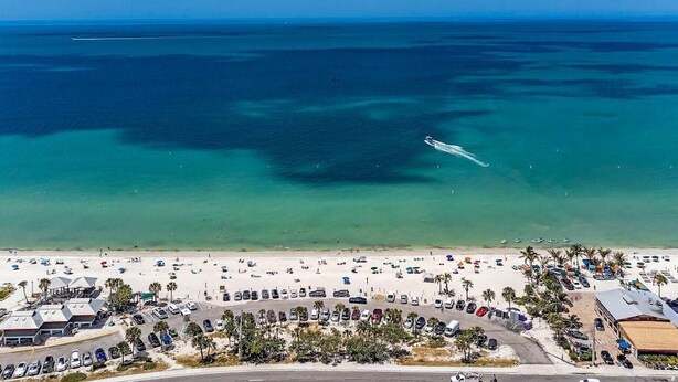 Luchtbeeld van een strand met een parkeerplaats, strandparasols en een helderblauwe lucht.