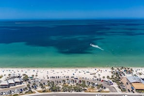 An aerial view of a beach with a parking lot, beach umbrellas, and a clear blue sky. - A Fully Remodeled Gulf Retreat — Stylish Comforts Steps from the Shore. (Bonita Springs)