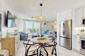 A modern kitchen with a dining area, a large refrigerator, and a balcony with a view. - A Fully Remodeled Gulf Retreat — Stylish Comforts Steps from the Shore. (Bonita Springs)