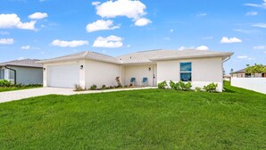Une maison de plain-pied avec un garage, une véranda abritée avec deux chaises et une pelouse bien entretenue.