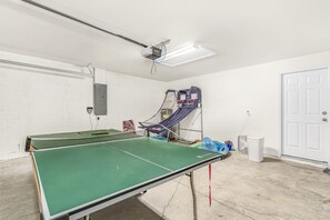 Una mesa de ping pong en una habitación con pared de ladrillo blanco, una puerta y un ventilador de techo.