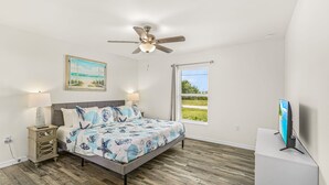 Une chambre à coucher avec un lit, des lampes de chevet, un ventilateur de plafond, un tableau, une fenêtre donnant sur un beau paysage et un téléviseur.