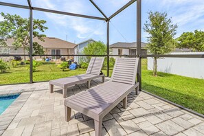 Ein überdachter Patio-Bereich mit zwei Liegestühlen und einem Schwimmbecken.