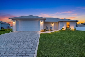 A residential house with a garage, a well-maintained lawn, and a driveway. - Cape Coral Retreat | Heated Pool, 2 King Suites & Dog-Friendly Game Room (Cape Coral)