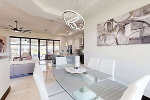 Eine moderne Küche mit einer großen Kücheninsel, ein Essbereich mit Glastisch und ein Wohnbereich mit Sofa.