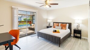 Ein Schlafzimmer mit Bett, Nachttischen, Deckenventilator und Blick auf einen Pool durch eine Schiebetür.