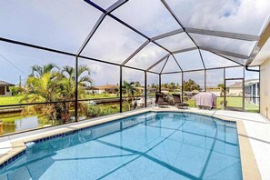 A covered swimming pool with a view of a residential area. - Waterfront home with screened pool, patio, grill, foosball, AC, & W/D (Cape Coral)