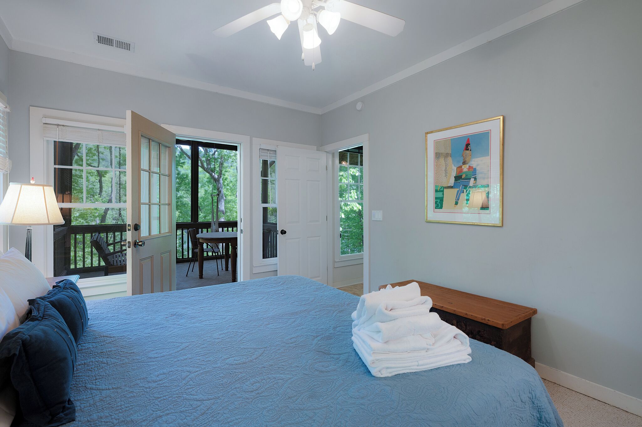Une chambre à coucher comprenant un lit, un bureau, une chaise, un ventilateur de plafond et un tableau accroché au mur.